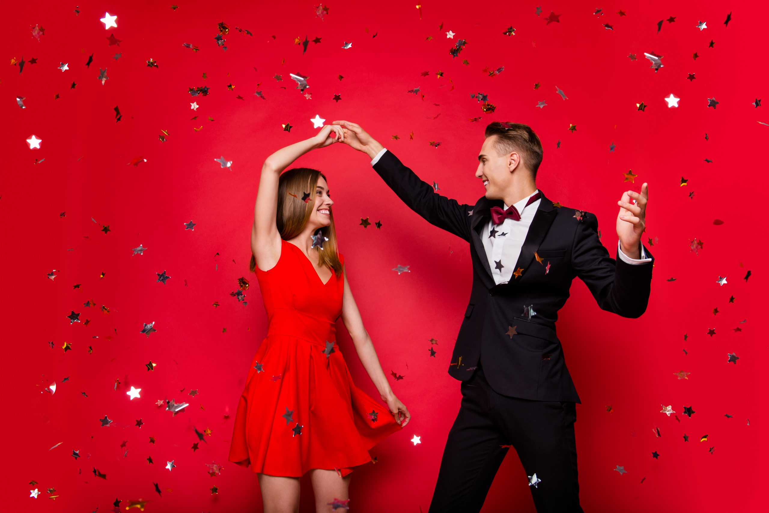Portrait of two cool slim graceful adorable imposing attractive cheerful people friends rejoicing flying decorative elements glitter having fun isolated over bright vivid shine red background